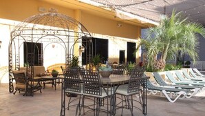 An outdoor patio with a round table and chairs, a covered seating area, and lounge chairs.