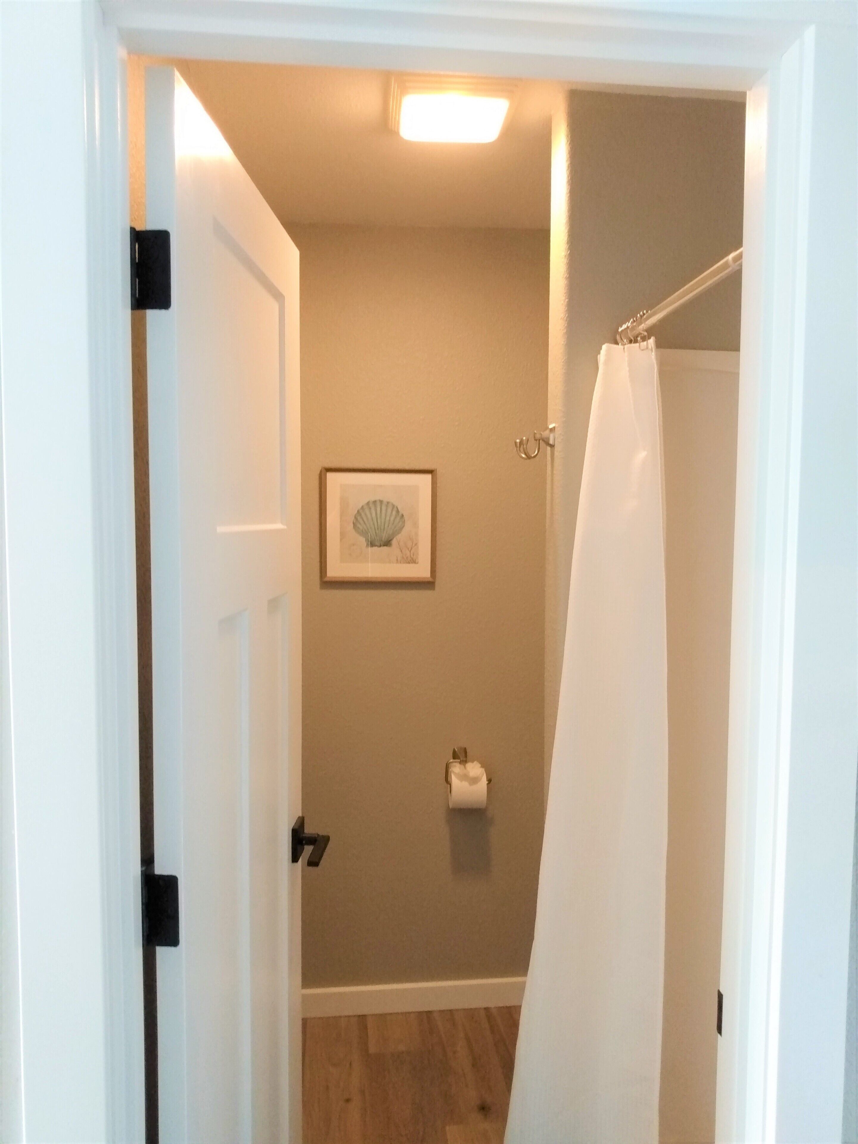 Une salle de bain avec un rideau de douche, un tableau encadré au mur et un porte-rouleau de papier toilette.