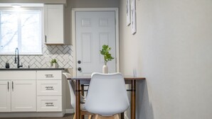 Una cocina con armarios blancos, salpicadero de azulejos, una mesa de comedor de madera con sillas y una planta en maceta.