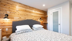 Ett sovrum med en väggpanel av trä, en säng med mönstrat sänglinne, två sänglampor och en dörr.