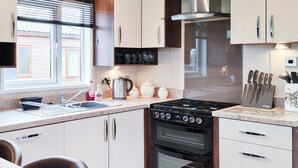 Una cocina moderna con estufa a gas, horno y electrodomésticos de acero inoxidable. Hay una ventana con persianas, un fregadero y una encimera con utensilios de cocina.