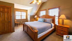 A bedroom with a wooden bed, two bedside tables with lamps, a ceiling fan, and a window with blinds. - 6BR Branson Lodge | 6 King Rooms | Near Silver Dollar City + Pools (FHL-263WO) (Branson)