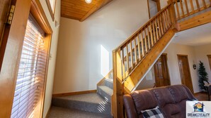 A staircase with wooden railings leading to a second floor, carpeted steps, and a view of the outside through a window with blinds. - 6BR Branson Lodge | 6 King Rooms | Near Silver Dollar City + Pools (FHL-263WO) (Branson)