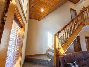 Eine Treppe mit Holzgeländern führt zu einer zweiten Etage, die Stufen sind mit Teppich belegt und durch ein Fenster mit Jalousien ist ein Blick nach draußen möglich.