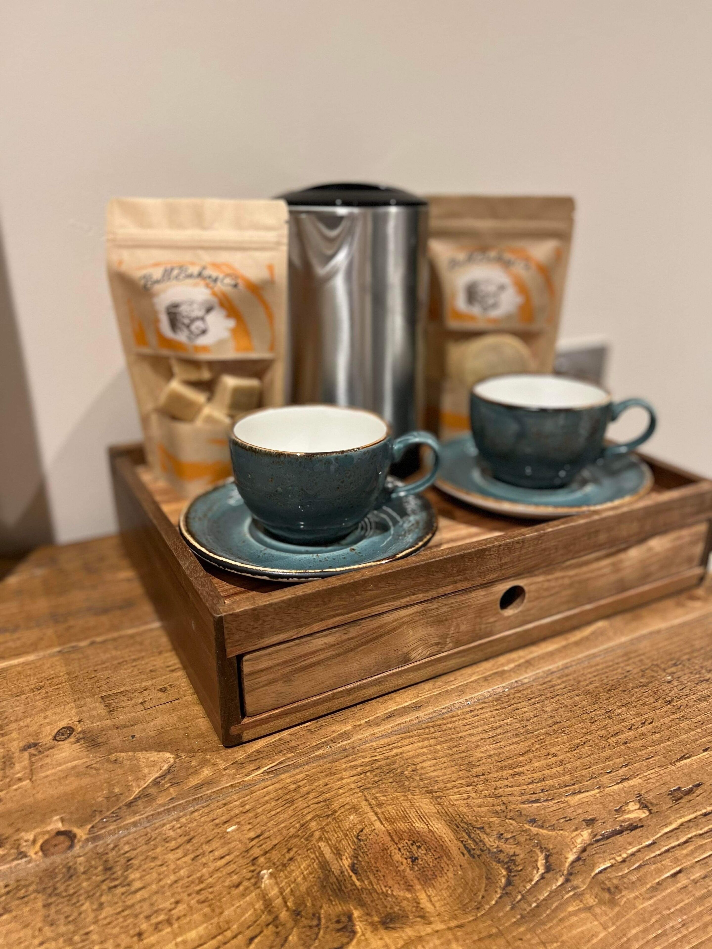A wooden tray with two ceramic cups and a thermos, placed on a table.