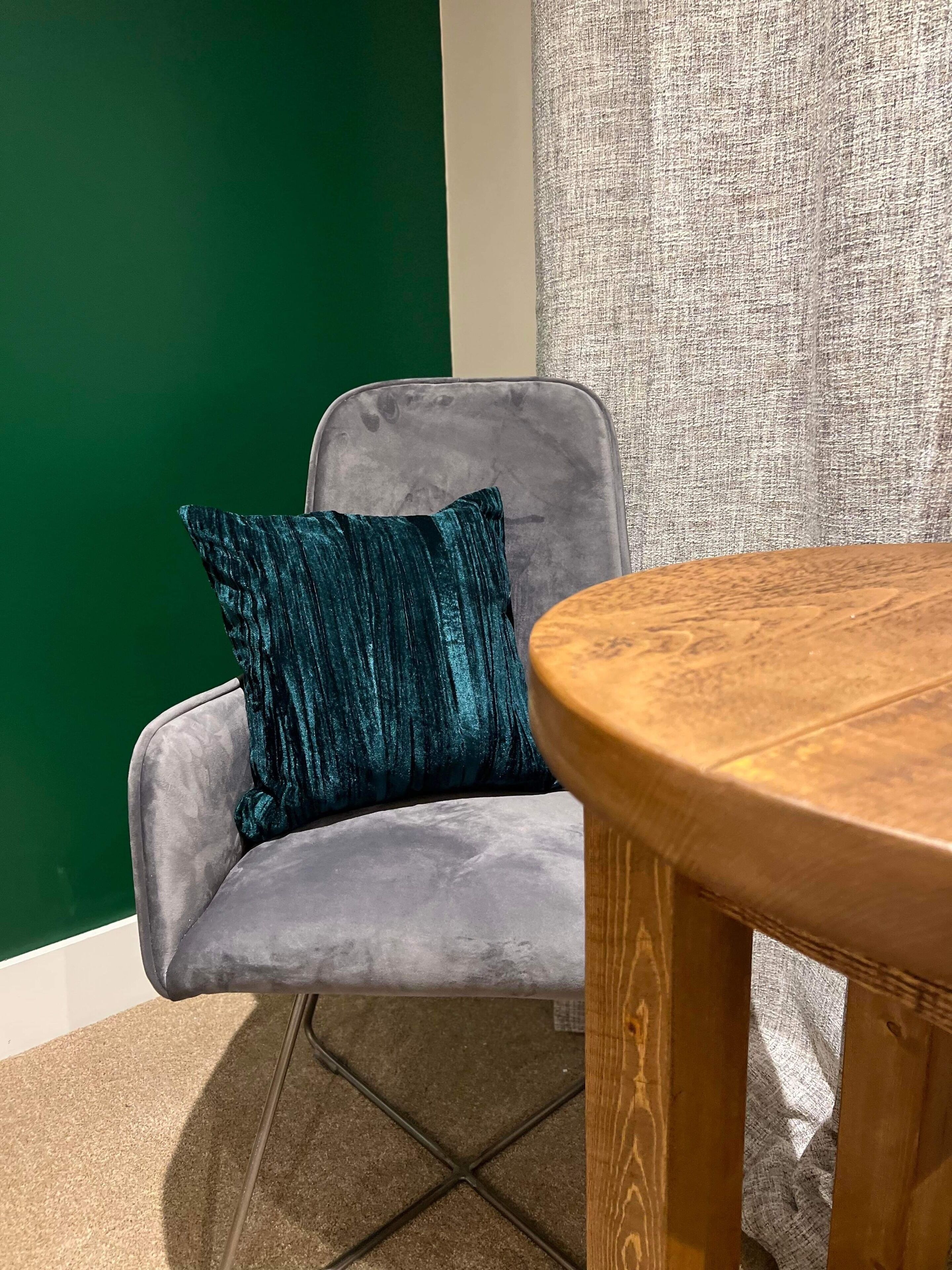 Un sillón gris con un cojín azul verdoso, una mesa de madera y una pared verde.