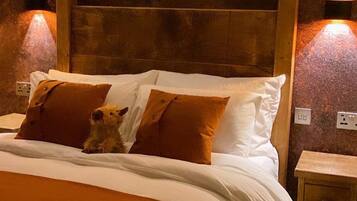 Un dormitorio con cabecera de madera, dos lámparas de noche, un perro en la cama y una manta marrón.