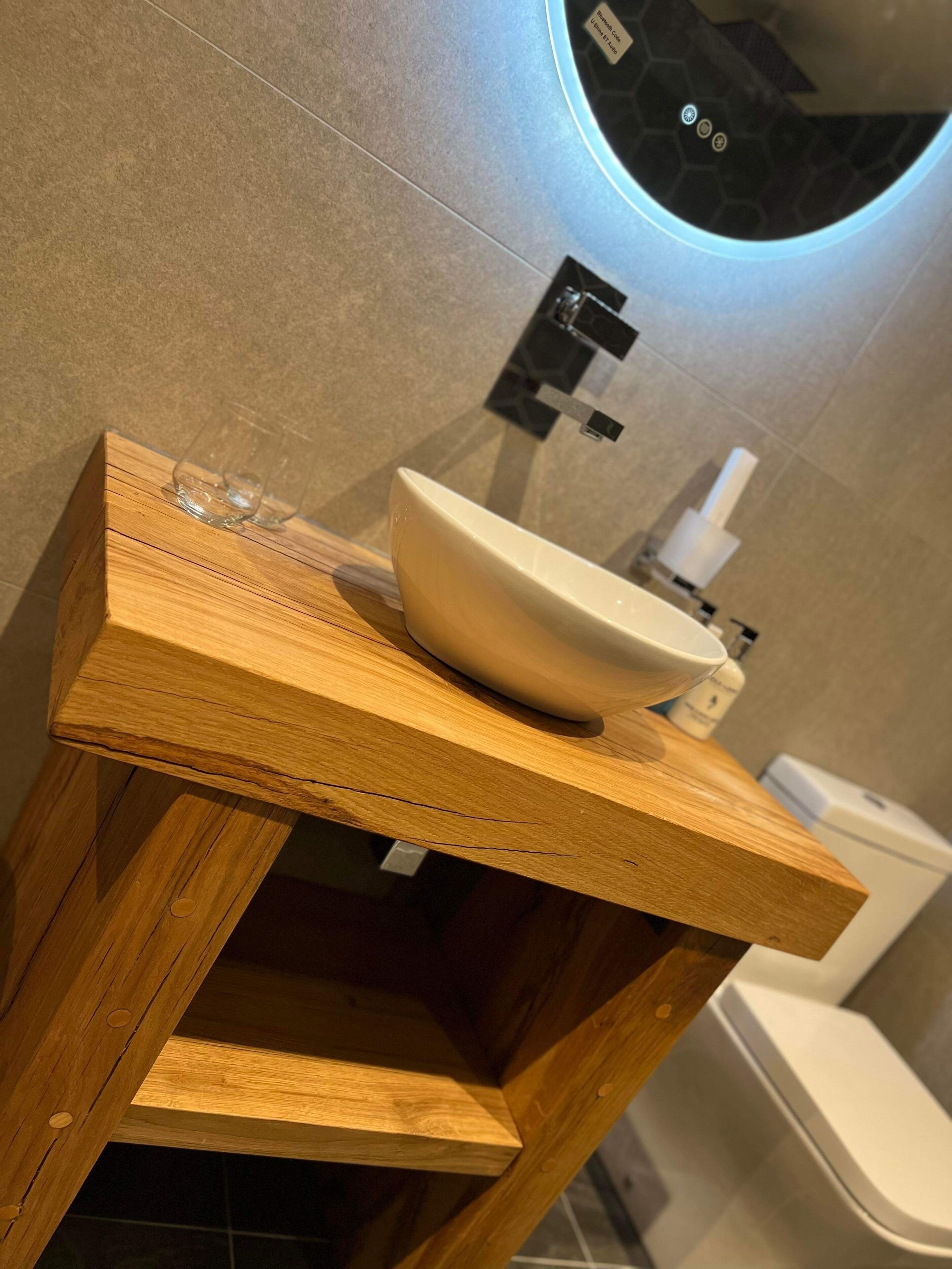 A wooden vanity with a white sink, a mirror, and a toilet in the background.