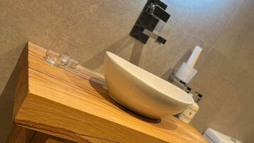 A wooden vanity with a white sink, a mirror, and a toilet in the background.