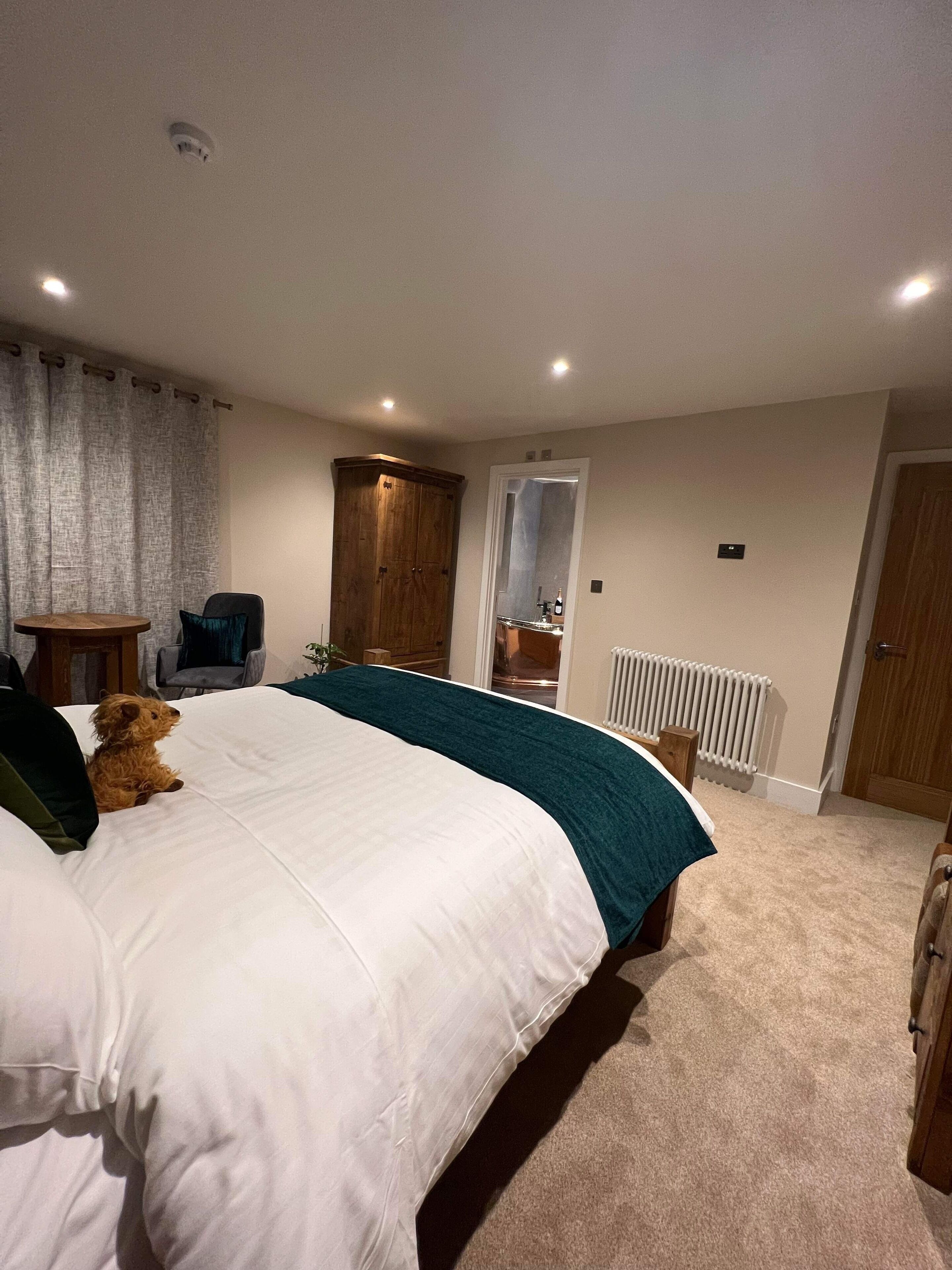 A bedroom with a large bed, a wooden wardrobe, a chair, a small table, and a radiator.