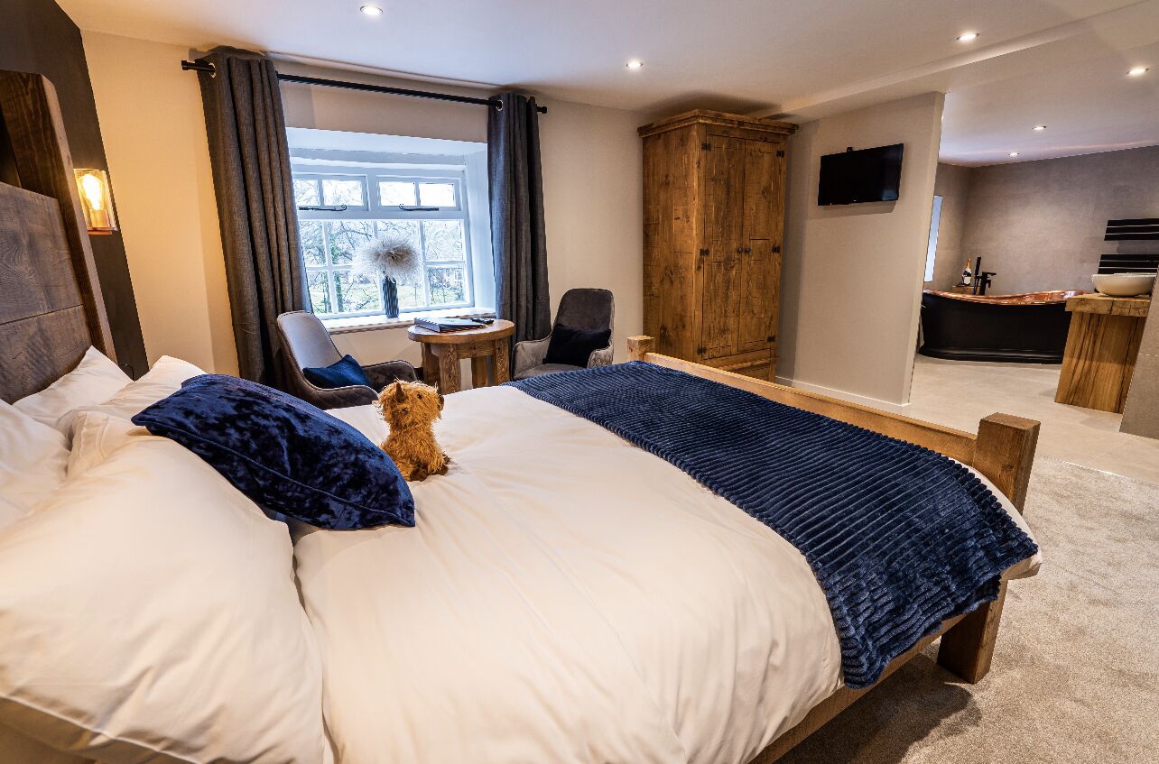 A hotel room with a large bed, a wooden wardrobe, a desk with a chair, and a television mounted on the wall.