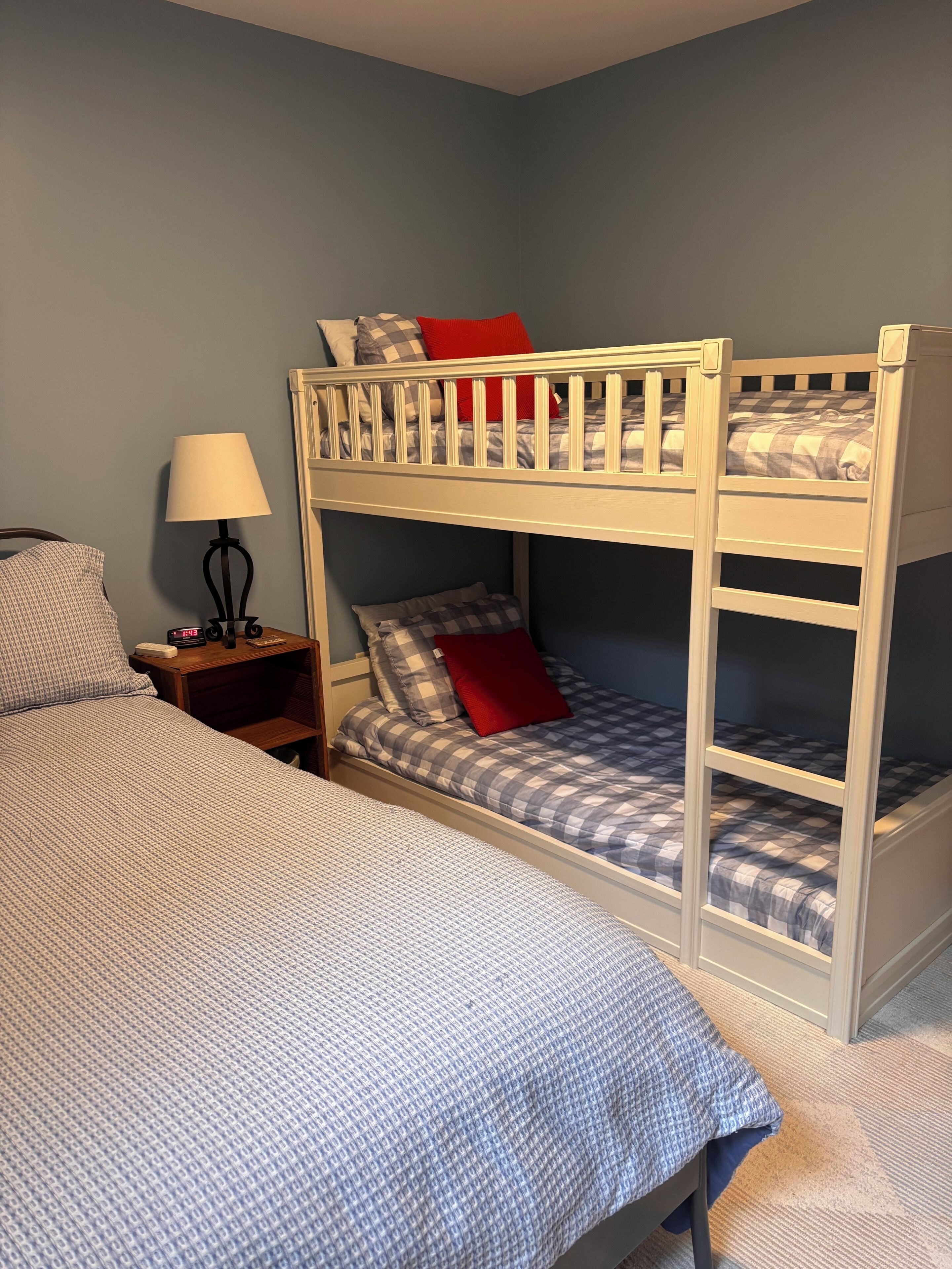 A bunk bed with a checkered bedspread, a nightstand with a lamp, and a wall clock.