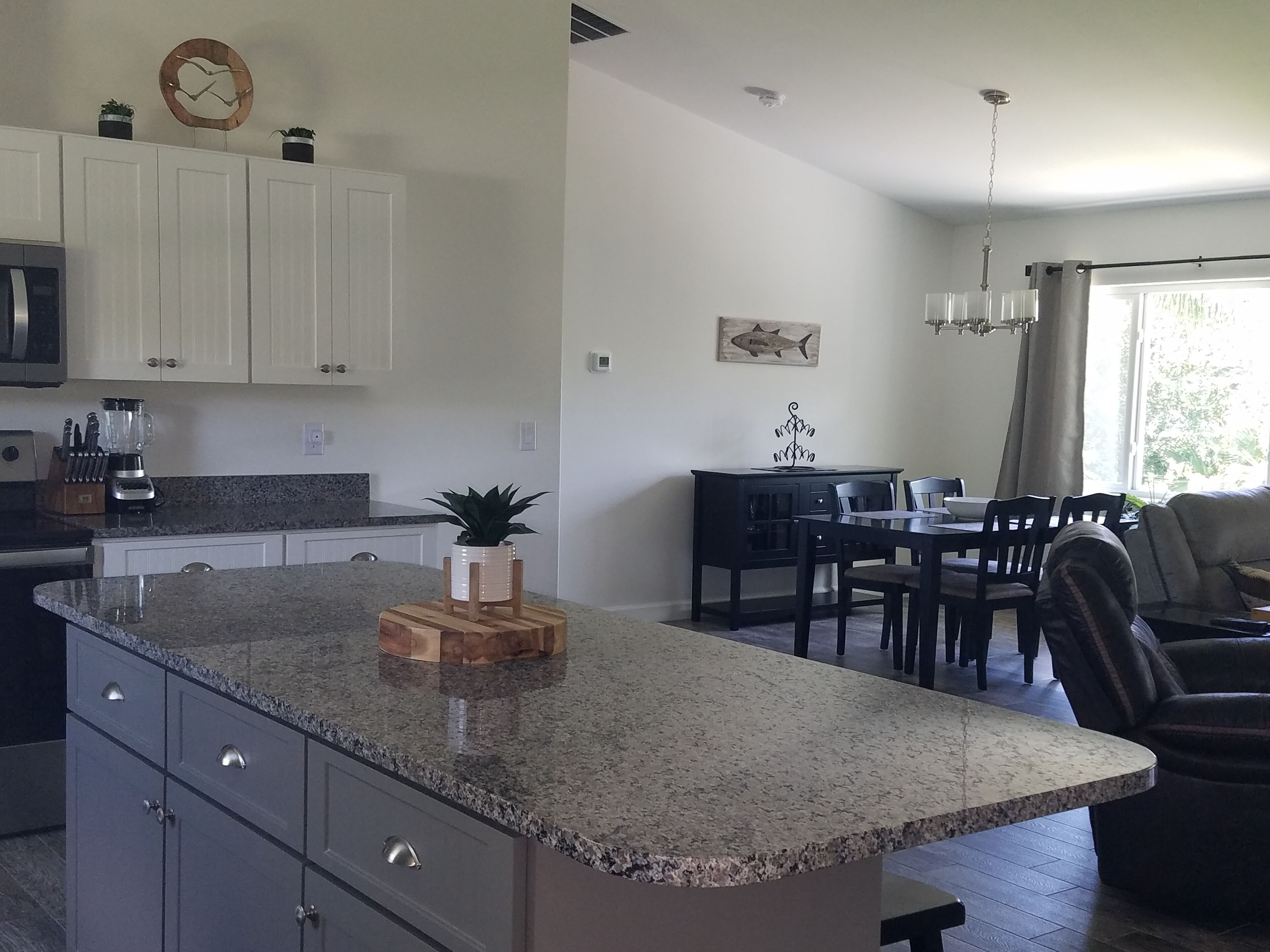Una cocina moderna con encimeras de granito, armarios blancos y un comedor con candelabro.