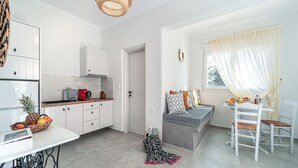 Una cocina moderna con armarios blancos, un comedor con mesa y sillas, y una zona de estar acogedora con cojines.