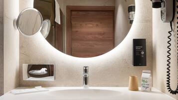 Un baño moderno con un espejo redondo, un lavamanos empotrado, un secador de pelo y un perchero para toallas.