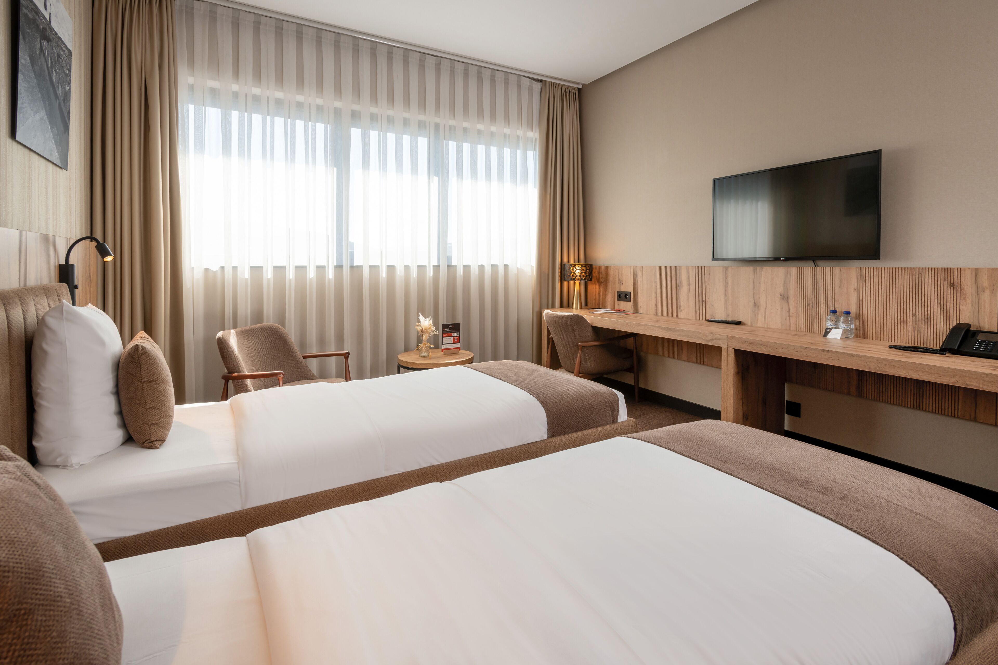 Habitación de hotel con dos camas, un escritorio, una silla, un televisor y una ventana con cortinas.
