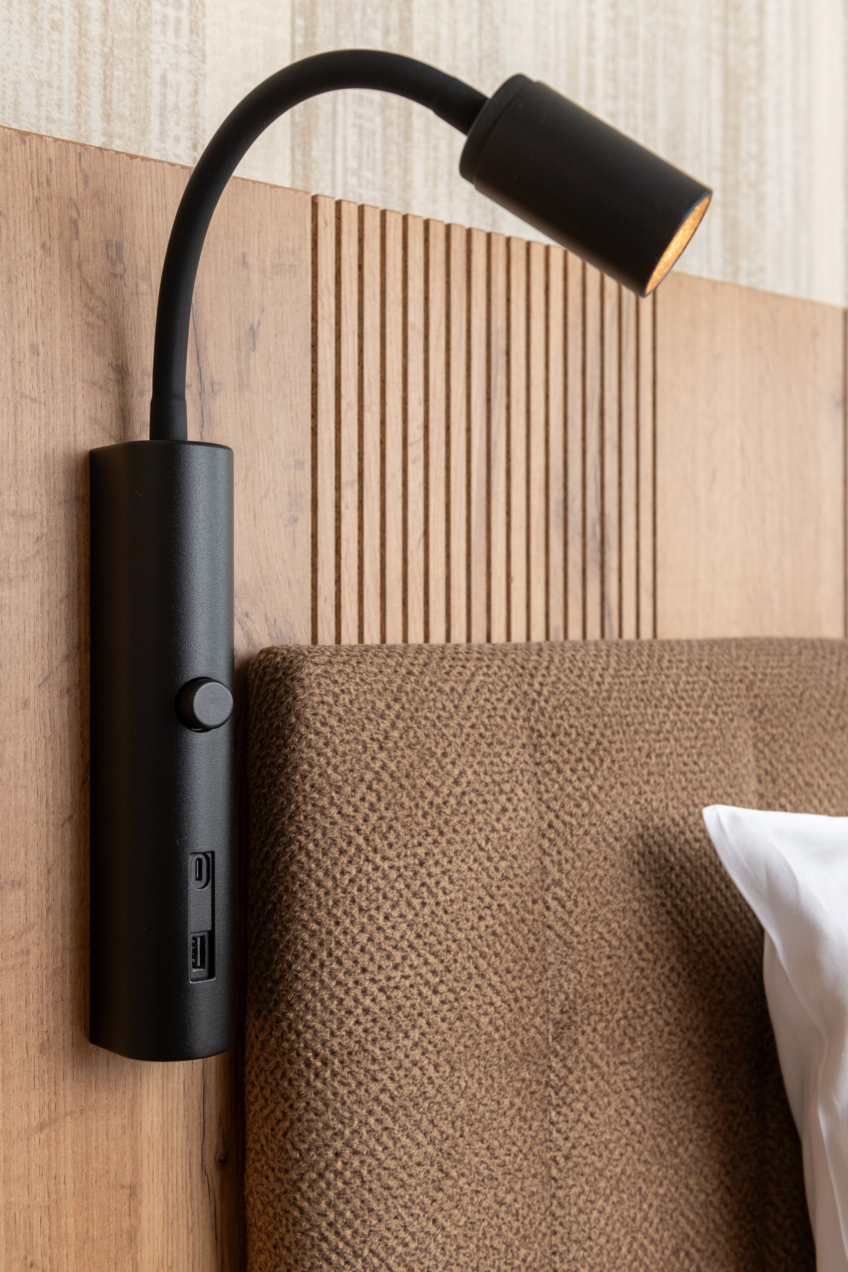 A wall-mounted lamp with USB ports, a textured brown sofa, and a wooden panel with vertical lines.