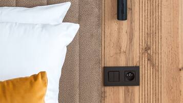 Una cama con almohadas blancas y mostaza, cabecera de madera, mesita de noche con cajón y aplique de pared.