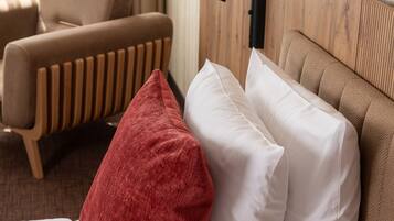 A hotel room with a bed, a red and white pillow, a wooden headboard, a bedside lamp, and a window with curtains.