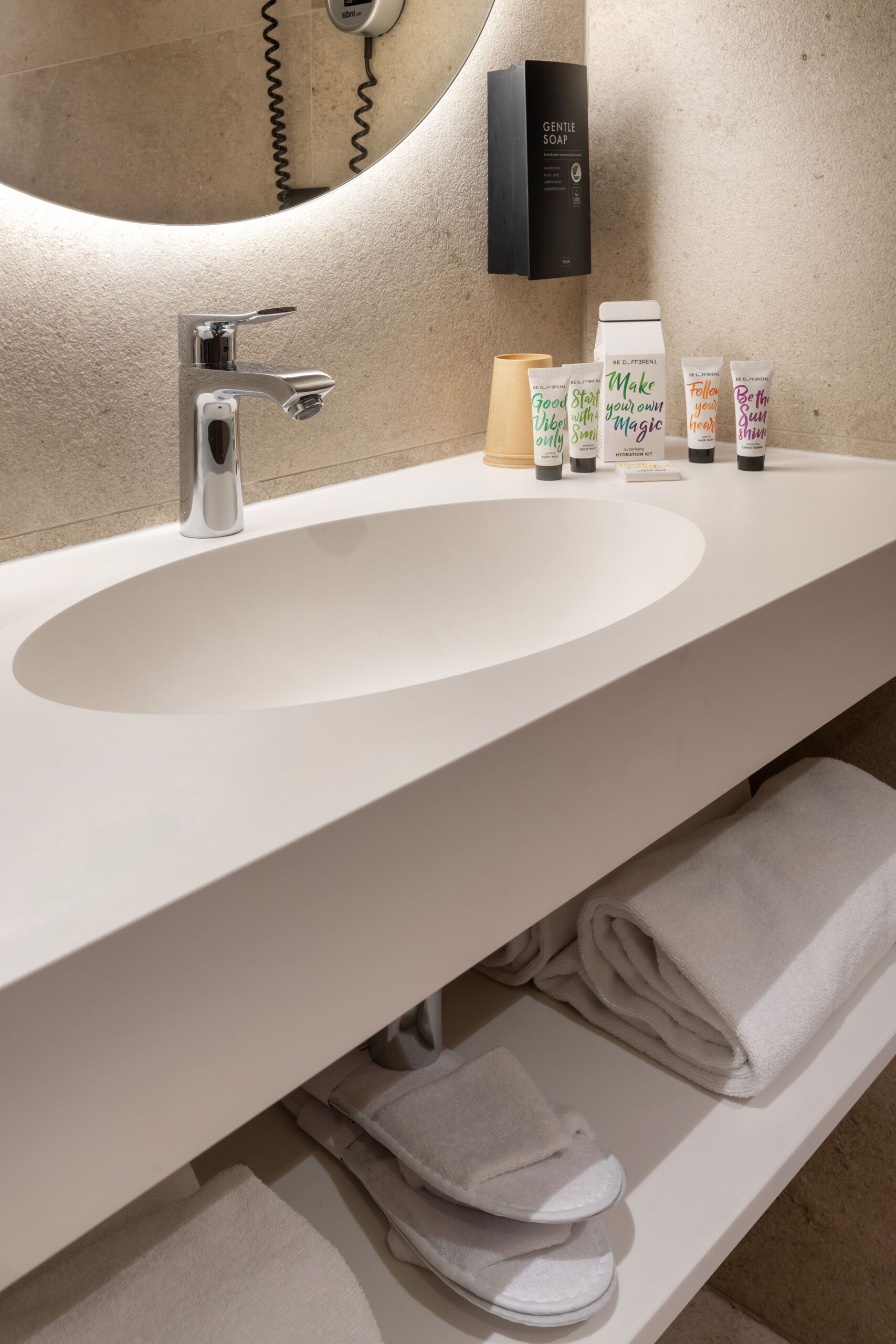 A modern bathroom with a large sink, a mirror, a towel rack, and a bottle of Gentle Soap.