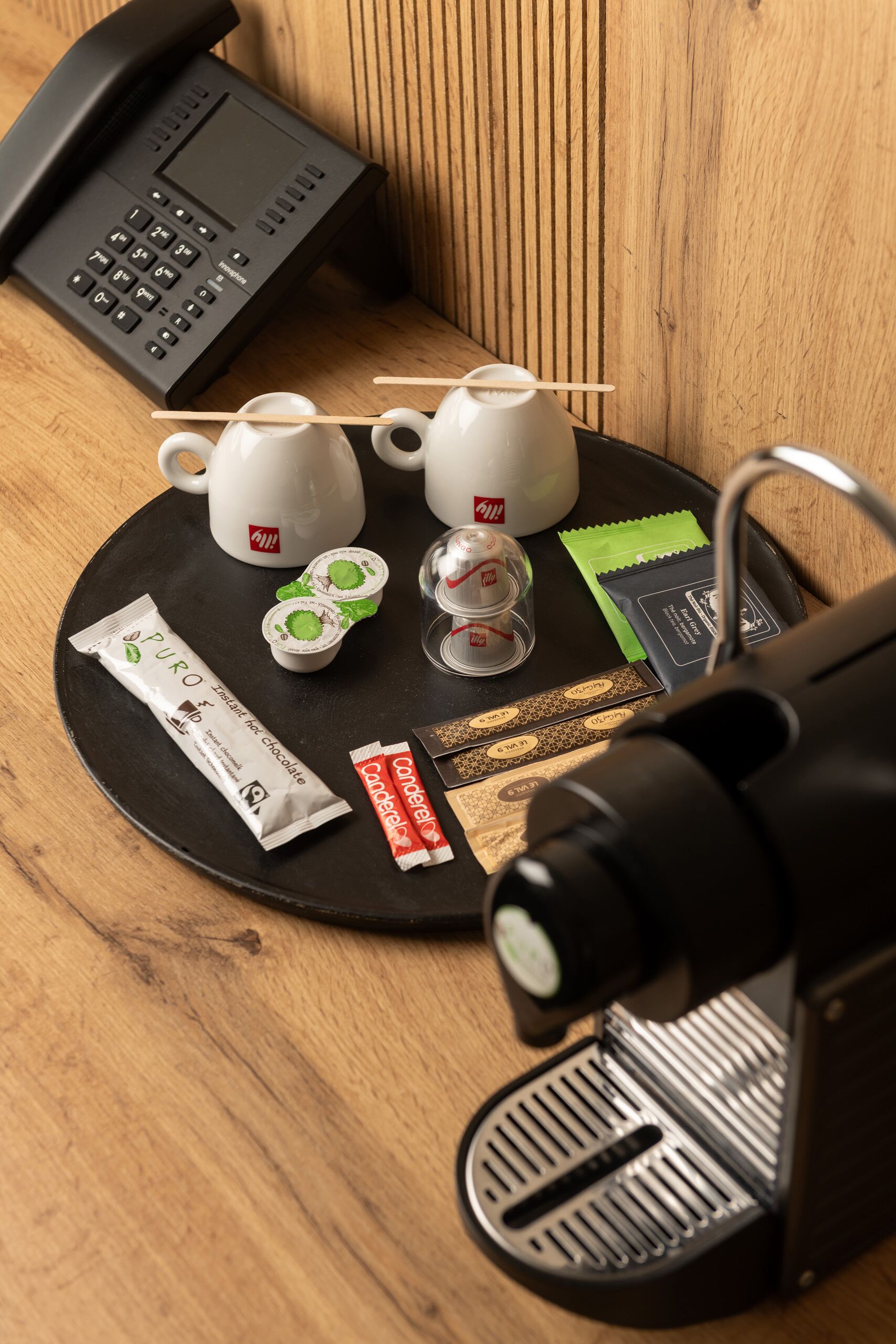 Un angolo con una macchina da caffè, due tazze, un telefono e qualche snack su un vassoio.