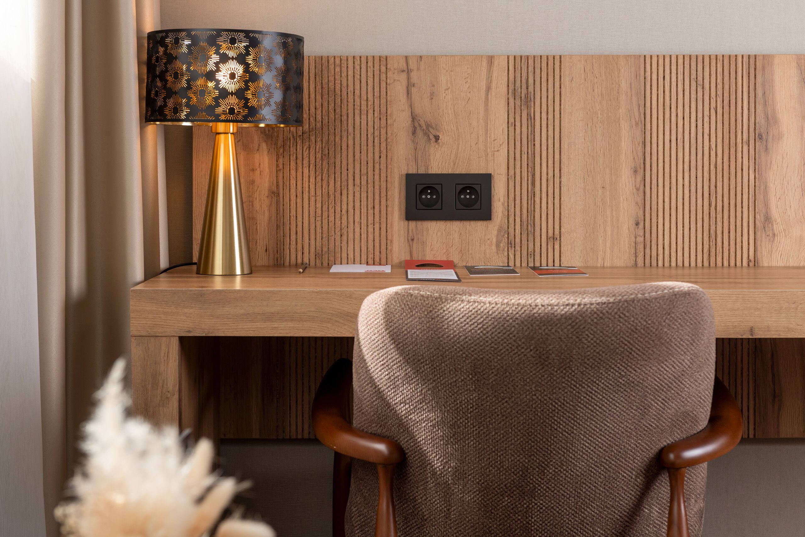 A wooden desk with a lamp, two wall sockets, and a chair.