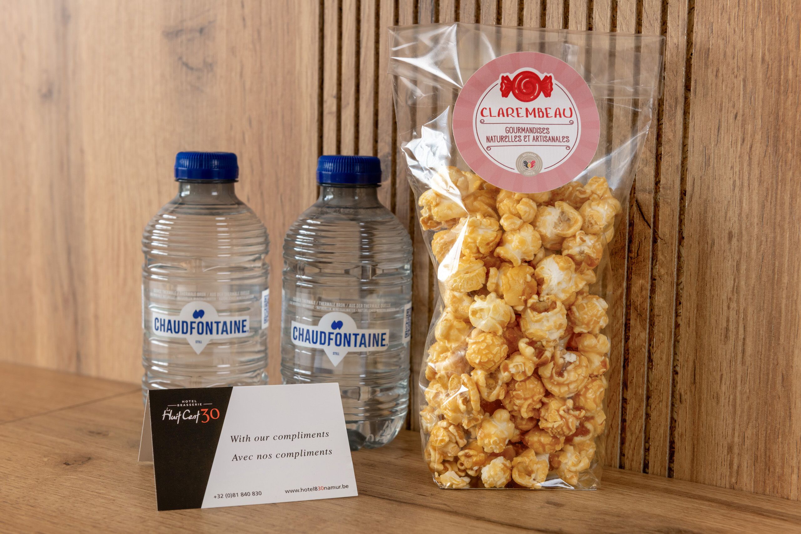 Due bottiglie d'acqua Chaud Fonteine, una confezione di snack gourmet Clarembeau e un biglietto di benvenuto dell'hotel.
