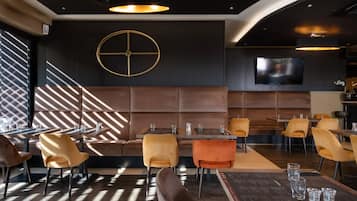 A modern restaurant with a central seating area, multiple tables, and a large TV screen.
