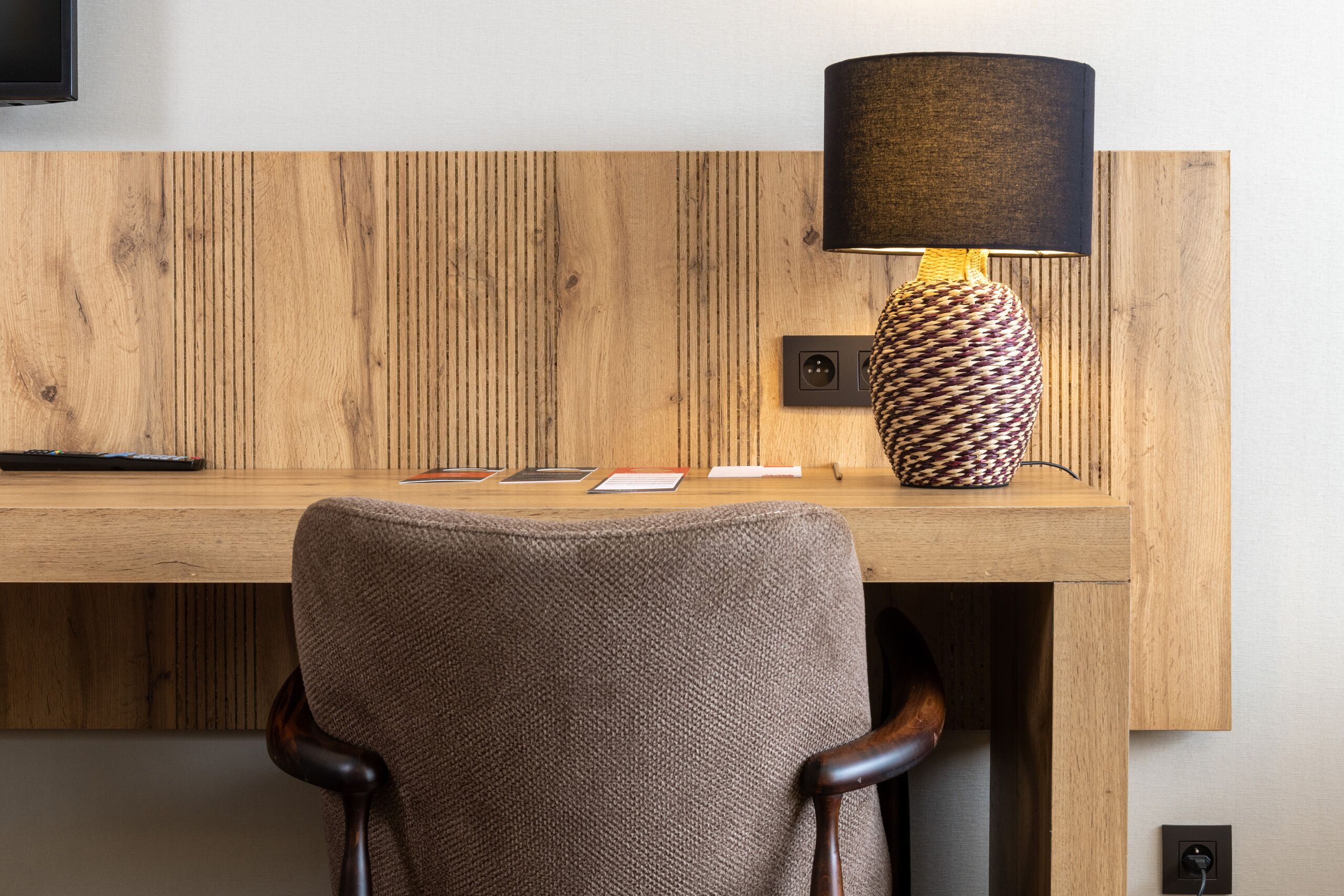 Een houten bureau met een lamp, papieren en een stoel.