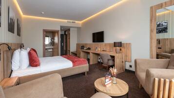 A hotel room with a bed, a desk, a TV, a chair, and a sofa.