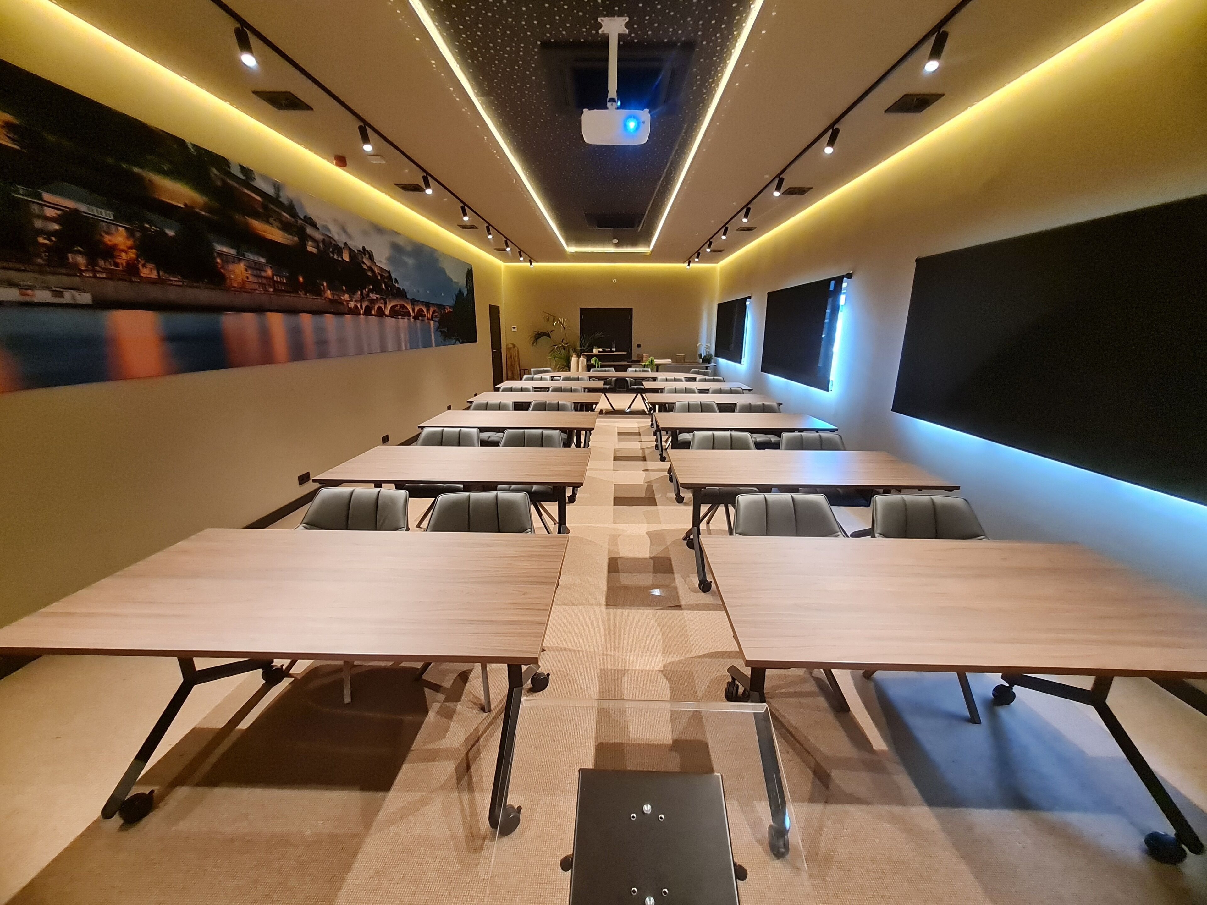 Een congreszaal met rijen tafels en stoelen, een projecteerder en een groot scherm aan de muur.
