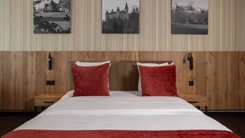 A hotel room with a wooden panel wall, a large bed with red pillows, and three black-and-white photographs on the wall.