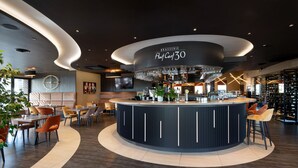 Zona de bar moderna con barra circular, asientos alrededor y una gran lámpara de candelabro.