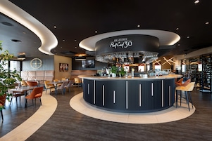 Zona de bar moderna con barra circular, asientos alrededor y una gran lámpara de candelabro.