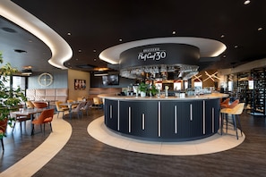 A modern bar area with a circular counter, seating around it, and a large chandelier.