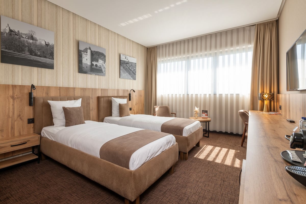 Une chambre d’hôtel avec deux lits, un bureau, une chaise et un téléviseur.