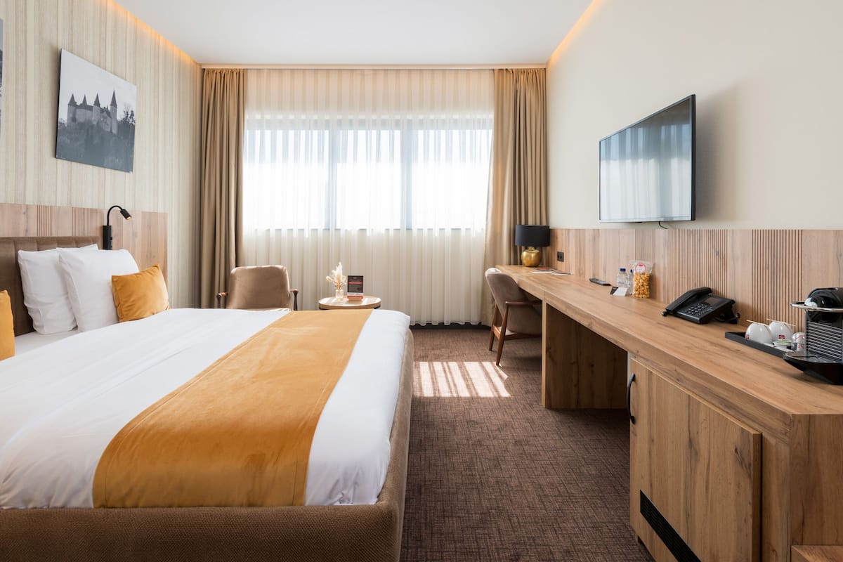 Une chambre d’hôtel avec un grand lit, un bureau, une chaise, une télévision et une fenêtre avec des rideaux.