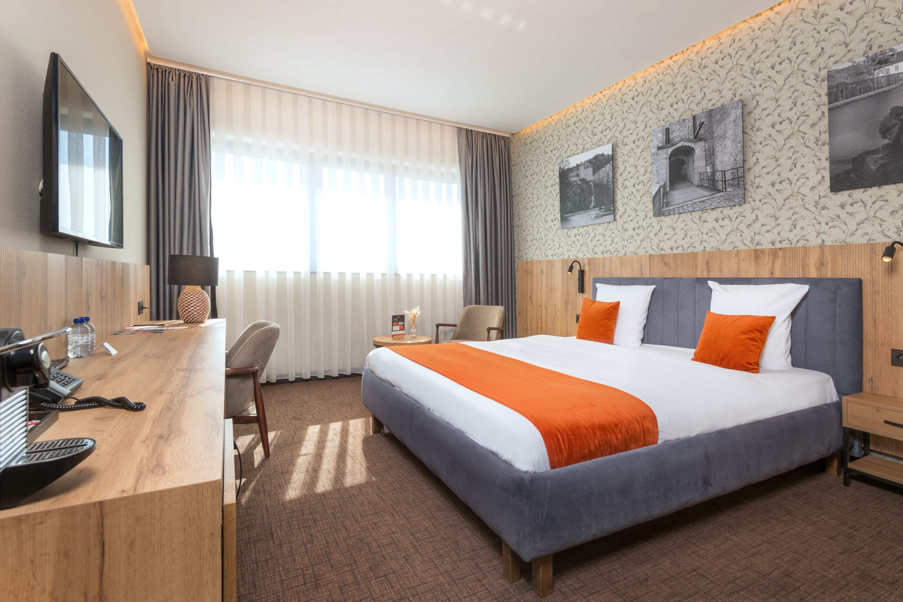Hotelkamer met een groot bed, een bureau met telefoon, een stoel, een televisie en een raam met gordijnen.