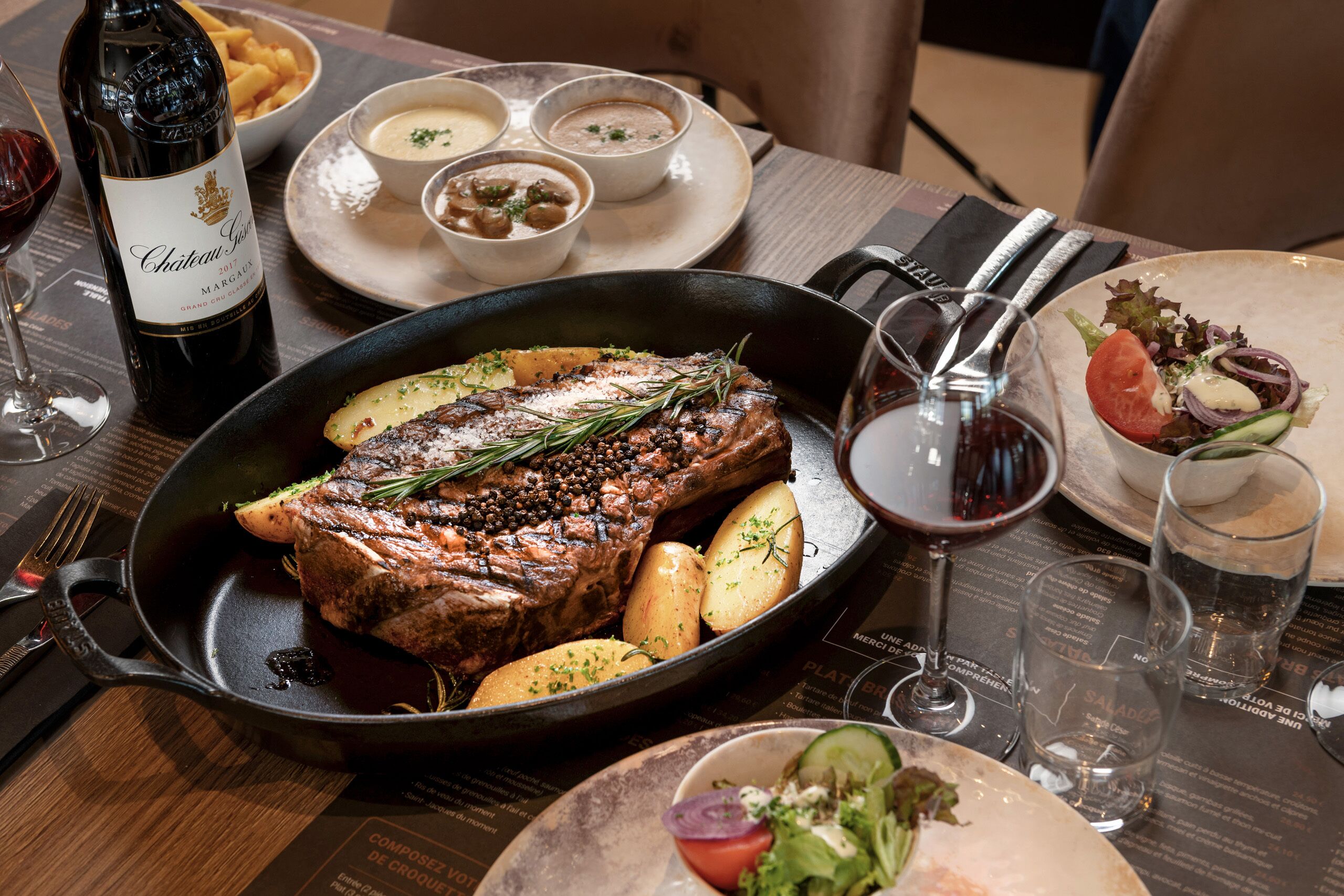 A steak with potatoes and a bottle of wine on a table.