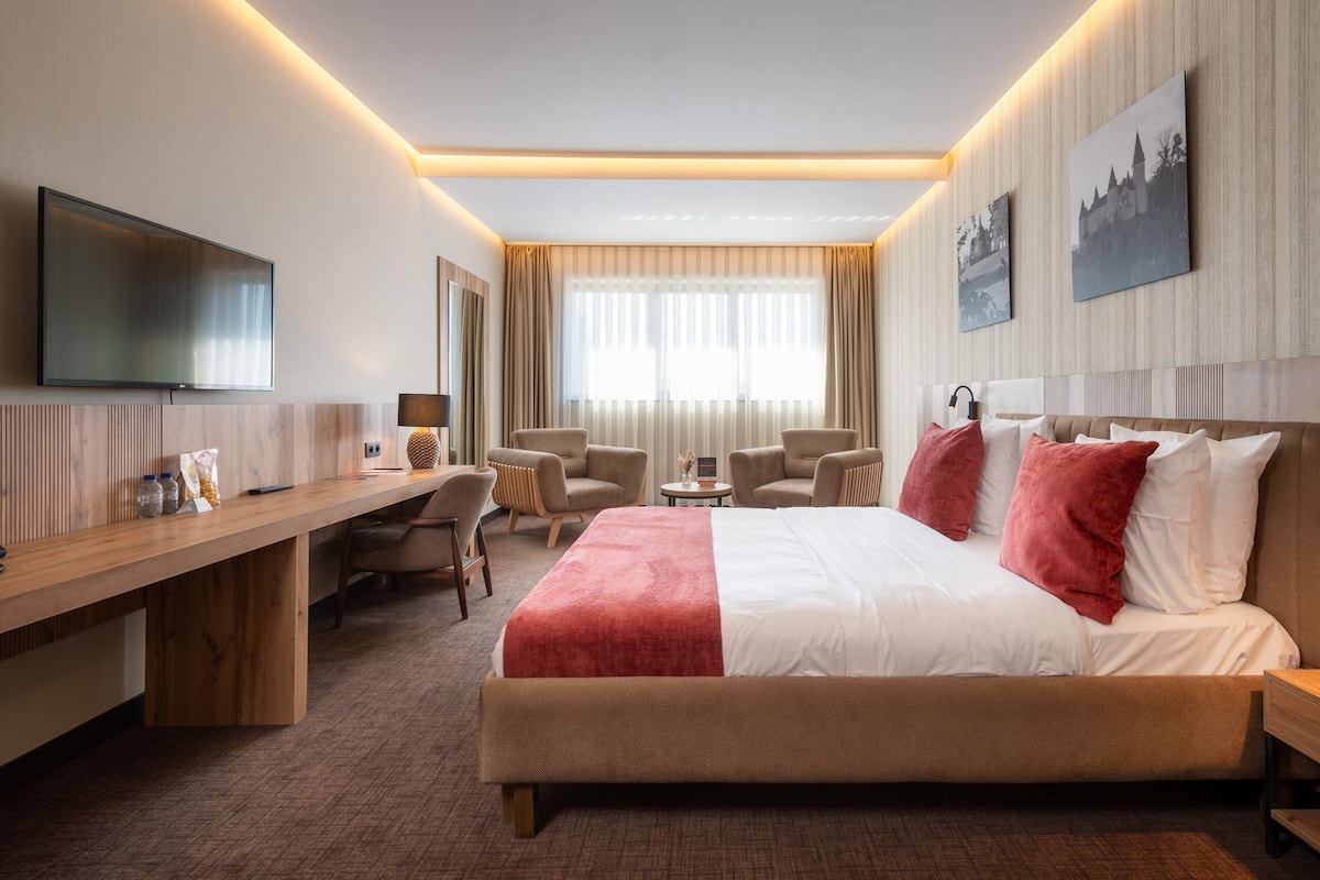 Une chambre d’hôtel équipée d’un lit, d’un bureau, de chaises, d’une télévision et décorée avec des œuvres d’art aux murs.