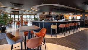A modern bar area with a curved counter, multiple seating options, and a large potted plant. - Hotel Le 830 (Namur)