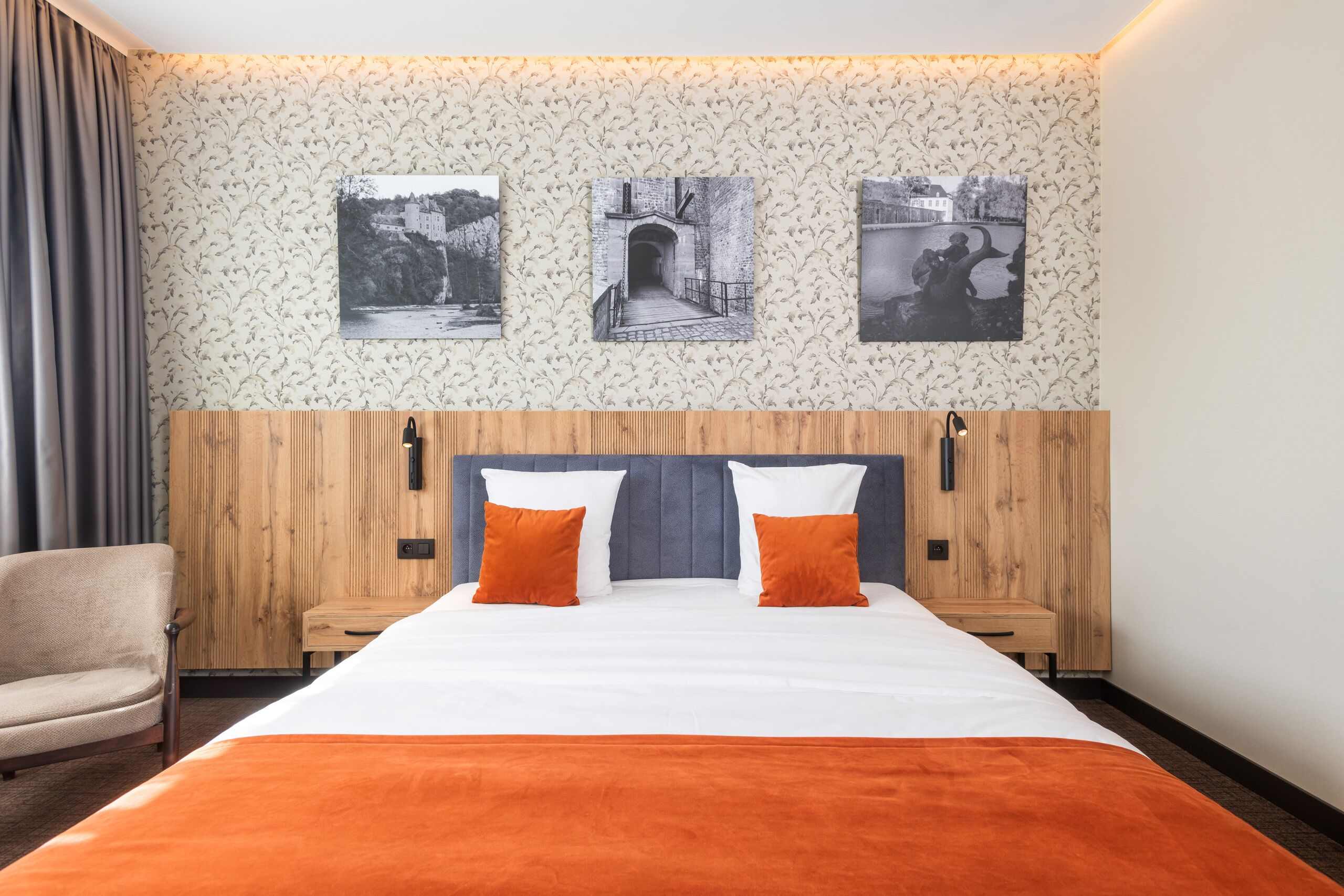 A hotel room with a bed, a chair, and three framed pictures on the wall.