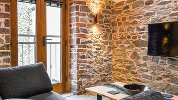 A cozy room with a stone wall, a wooden door, a flat-screen TV, a sofa, and a table with a bowl.