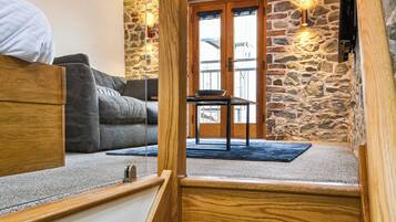 A cozy room with a stone wall, a wooden staircase, a gray sofa, and a small table with a bowl.