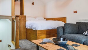 Een slaapkamer met een houten bed, een grijze bank, een houten tafeltje met een kom, en een hanglamp.