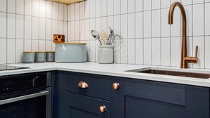 Een keuken met donkere kastjes, een wit aanrecht, een koperen kraan en een betegelde achterwand.