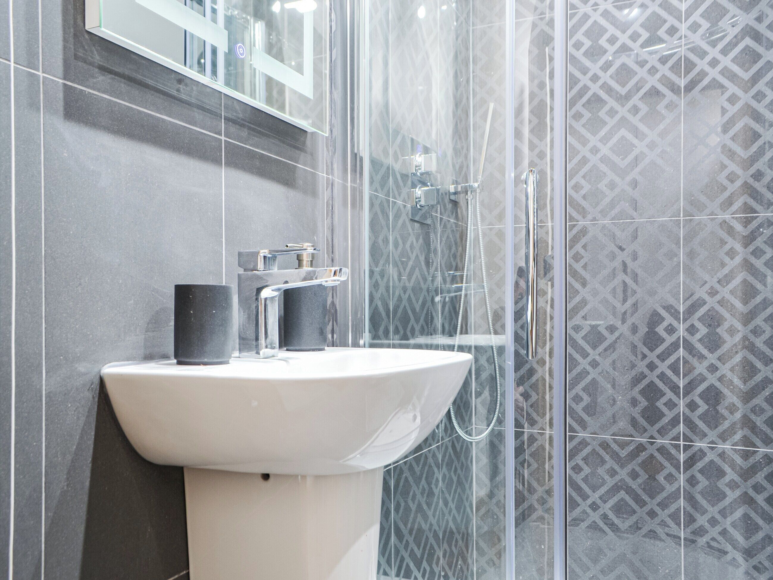 A bathroom with a white sink, a mirror, and a shower enclosure.
