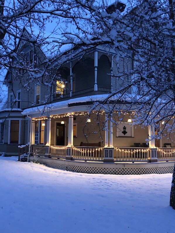 Ein zweistöckiges Haus mit Veranda, verziert mit Lichterketten, umgeben von Schnee.