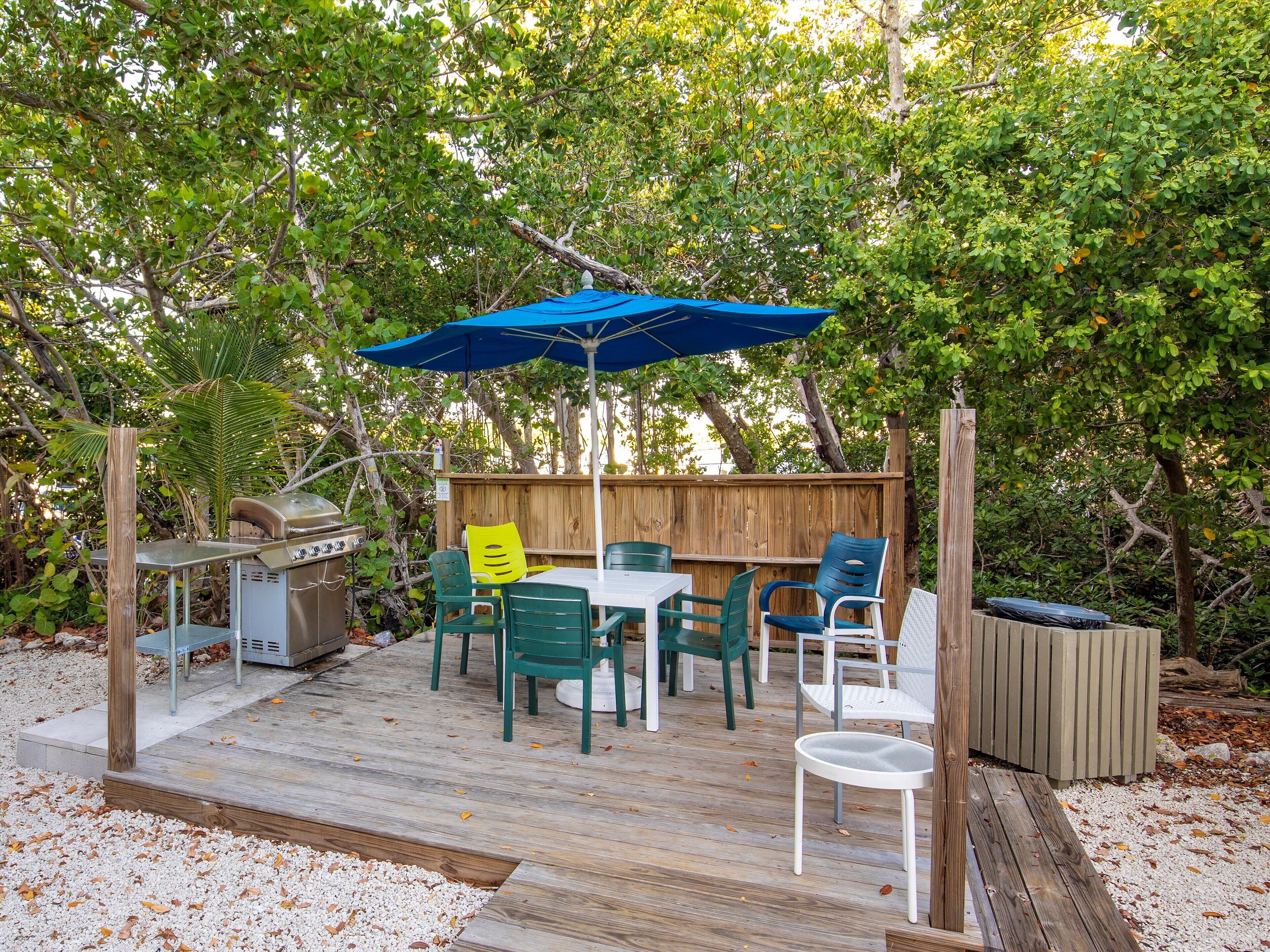 Une terrasse dotée d’un barbecue, d’une table et de chaises d’extérieur, ainsi que d’un parasol bleu.