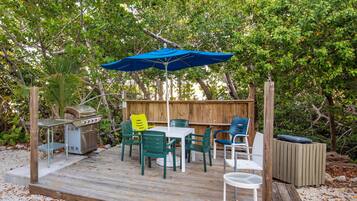 Une terrasse dotée d’un barbecue, d’une table et de chaises d’extérieur, ainsi que d’un parasol bleu.